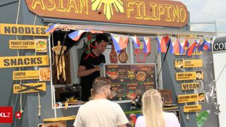 A Filipino food truck with a sign. A man serves food to two customers. The menu is displayed on a board.