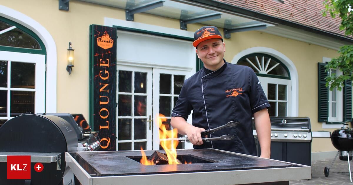 A chef stands by a grill with fire, wearing a cap and a blue shirt. The sign behind him reads 'GRILL LOUNGE'. He is holding tongs.