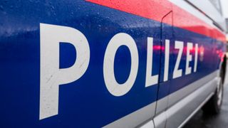 Ein Polizeifahrzeug mit blau-rot gestreiftem Design, das das Wort POLIZ in weißen Buchstaben zeigt. Die Oberfläche ist nass mit Wassertropfen.
