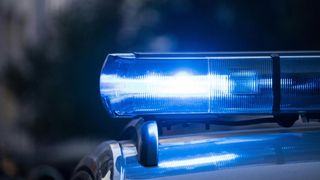 Das blaue Licht einer Polizeiautos erhellt die Nacht und signalisiert einen Notfalleinsatz. Der Schein des Lichts reflektiert sich auf der Fahrzeugoberfläche.