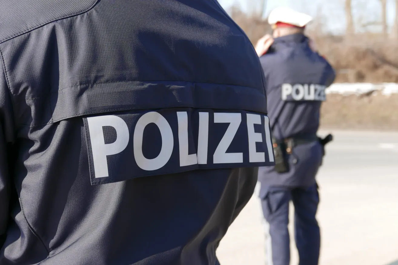 Ein Polizist in einer blauen Uniform steht hinter einem anderen Beamten in Uniform. Beide Beamte sind im Freien.