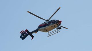 A police helicopter flies in the blue sky, with markings indicating it is OE-BXG.