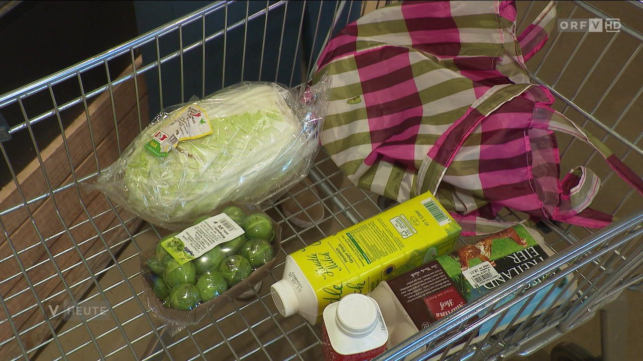 A shopping cart filled with various food items, including brussels sprouts, lettuce, and a carton of milk.