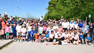 A group of people, likely a sports team, pose for a photo in an outdoor area with trees and a net in the background.