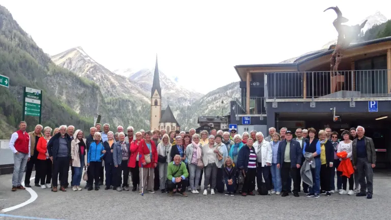 Eine große Gruppe von Menschen posiert für ein Foto vor einer Kirche in einem Gebirgsgebiet.
