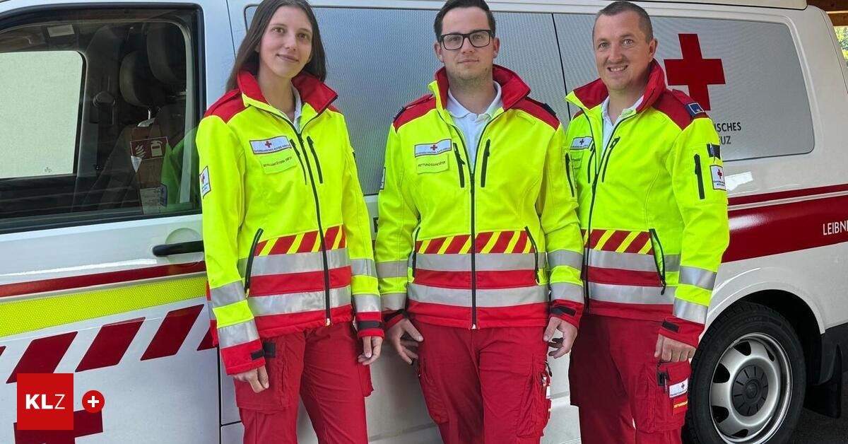 Drei Personen in Sicherheitsanzügen stehen vor einem Krankenwagen. Die Frau links hat lange Haare. Die beiden Männer tragen eine Brille und haben kurze Haare.