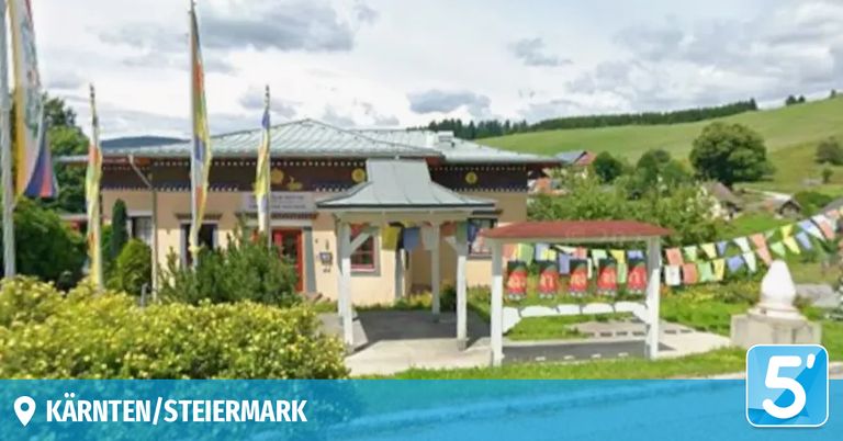 Ein Gebäude mit einem grauen Dach und Fahnen davor. Eine kleine Struktur mit einem roten Dach befindet sich in der Nähe. Das Gebiet ist von Grün umgeben. Die Worte 'Steiermark' sind prominent angezeigt.