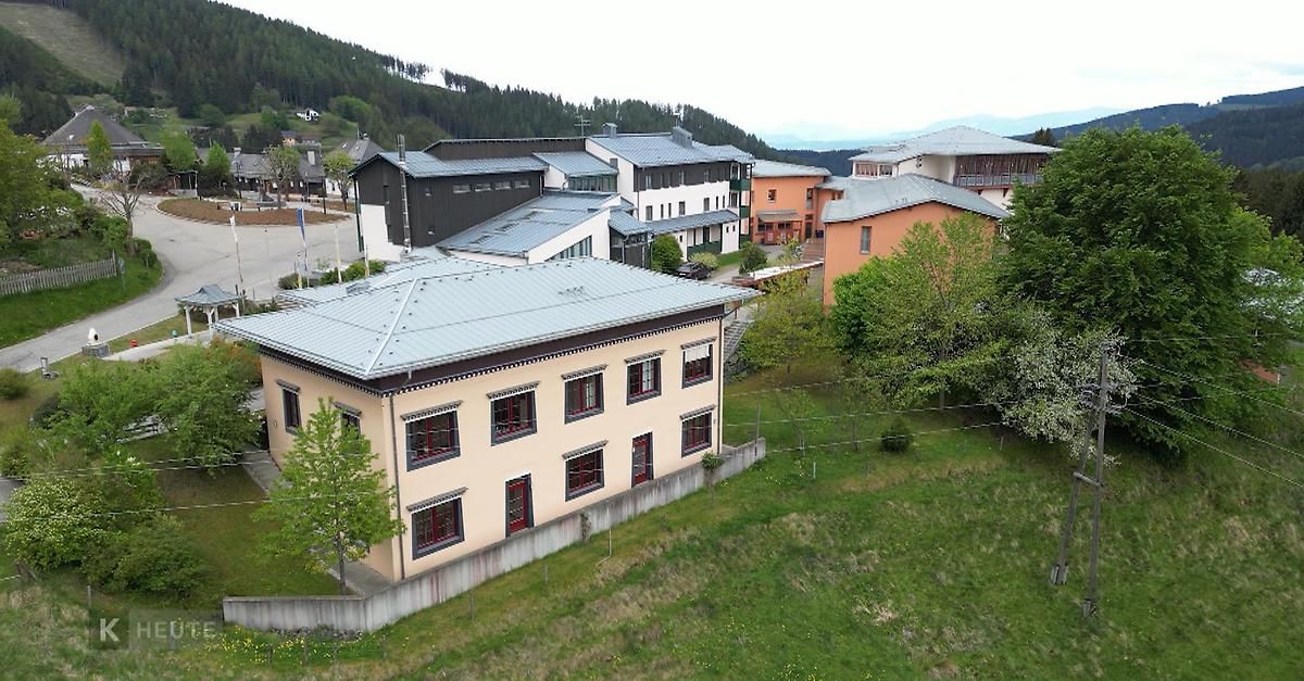 Ein Luftbild eines Wohngebiets mit einem Gebäude mit grauem Dach und roten Fensterrahmen. Bäume und Gras sind an den Seiten.