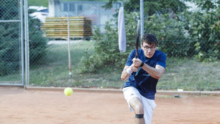 Ein Mann schwingt einen Tennisschläger und ist kurz davor, einen Tennisball auf einem Sandplatz zu treffen.