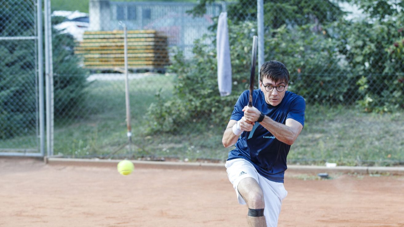 Ein Mann schwingt einen Tennisschläger und ist kurz davor, einen Tennisball auf einem Sandplatz zu treffen.