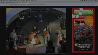 A live performance of Still Waters, featuring three musicians on stage with instruments and a crowd in the background.