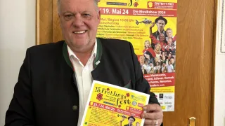 A man stands in front of a door with a poster advertising a festival, holding a flyer with more details about the event.