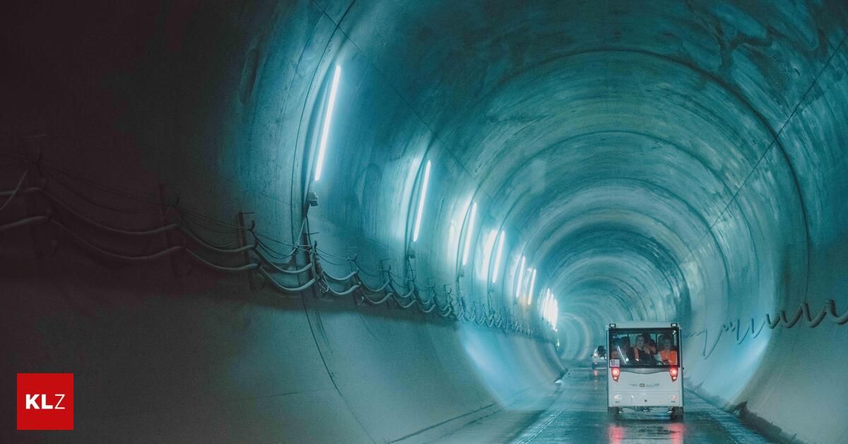 A small electric vehicle with passengers is driving through a tunnel with blue lighting.