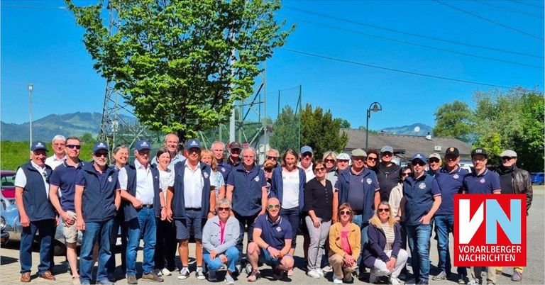 Eine Gruppe von Menschen in passenden Uniformen posiert für ein Foto vor einem Baum und einem Zaun mit Bergen in der Ferne.