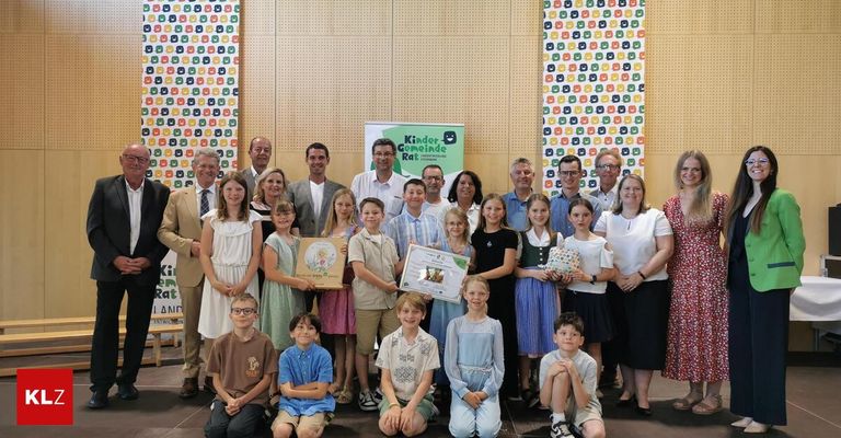Eine Gruppe von Erwachsenen und Kindern posiert für ein Foto in einem Raum mit buntem Hintergrund. Sie halten Urkunden und Geschenke in den Händen.