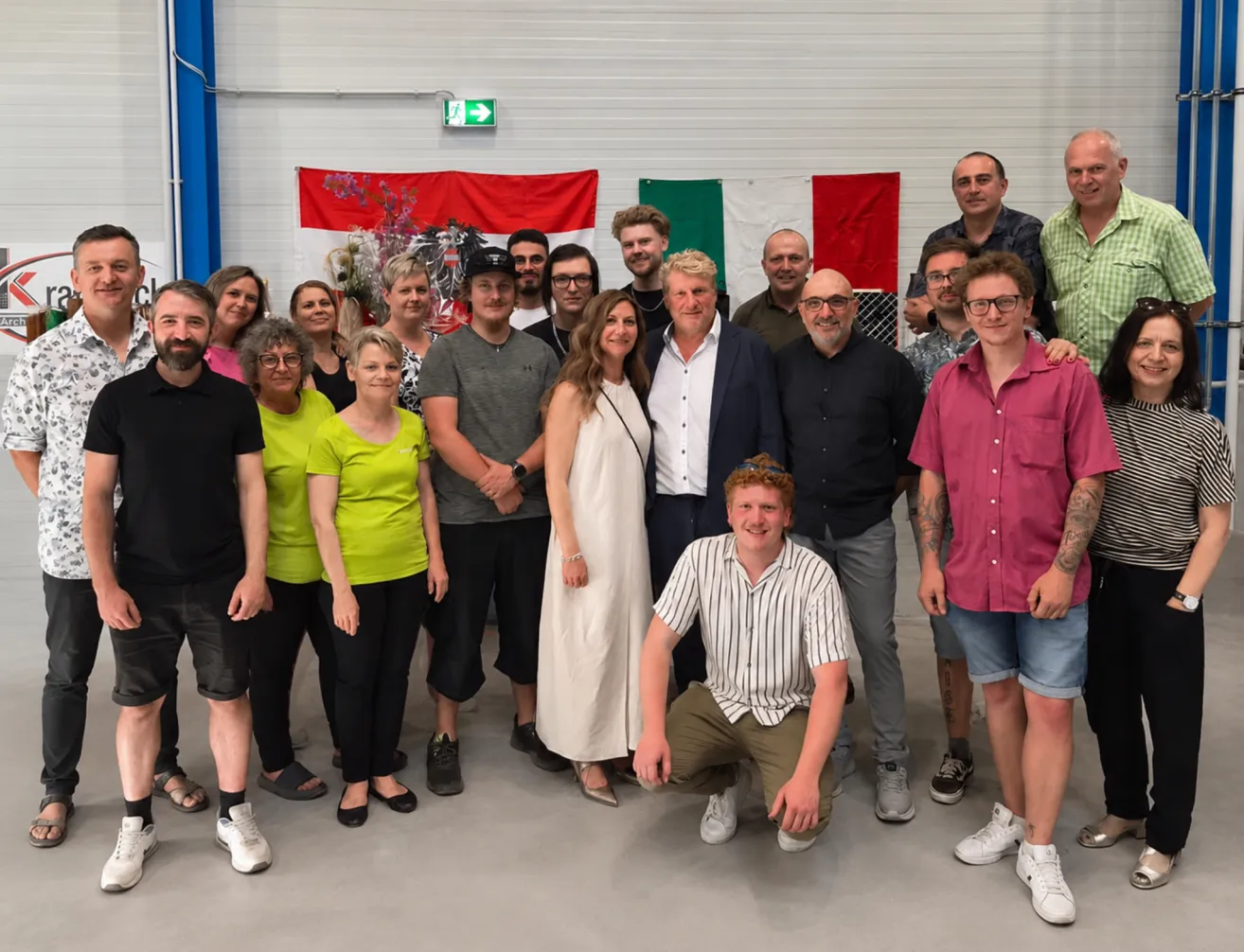 A group of people, including men and women, are posing for a photo in a room with flags on the wall.