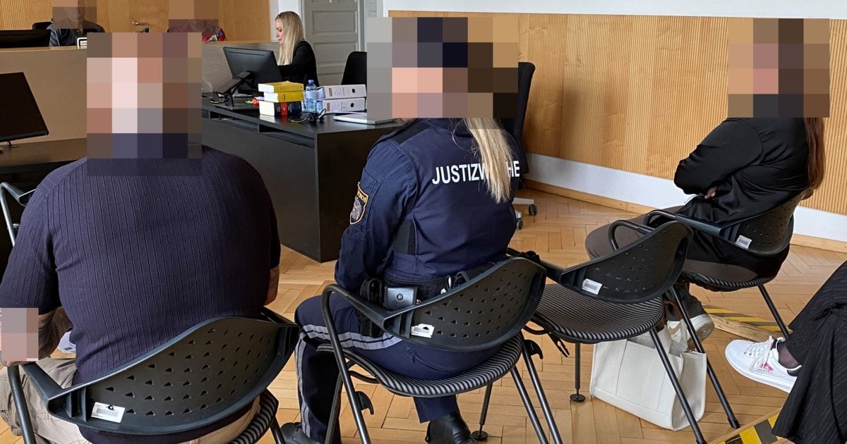 Eine Polizistin sitzt in einem Stuhl in einem Besprechungsraum, mit einer verschwommenen Frau, die im Hintergrund an einem Schreibtisch arbeitet.