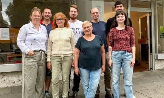 Eine Gruppe von Menschen steht vor einem Gebäude mit einem Schild, das 'Craft Club' steht. Sie scheinen für ein Gruppenfoto zu posieren.