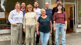 Eine Gruppe von Menschen steht vor einem Gebäude mit einem Schild, das 'Craft Club' steht. Sie scheinen für ein Gruppenfoto zu posieren.