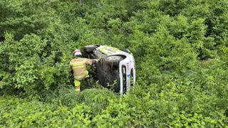 Ein Feuerwehrmann zieht ein weißes Auto aus einem Wald, mit zwei Reifen auf dem Boden und zwei auf dem Dach.