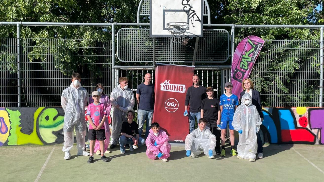 A group of people in protective gear pose for a photo in front of a basketball court. A red banner with the words AK Young is in the background.