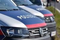 Three police vehicles are parked on a street, with the front vehicle displaying the word 'POLIZEI'. The vehicles have blue, red, and silver colors.