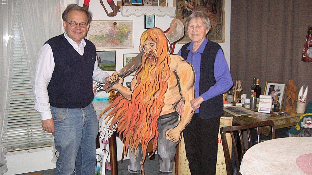 A man and a woman are standing next to a large wooden cutout of a bearded man with an axe. The man is holding the cutout.