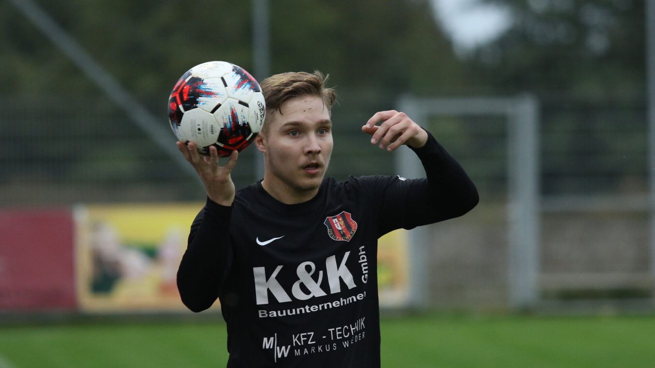 A man in a black soccer jersey holds a soccer ball in his hands on a field.