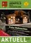 Ein Haus mit einer Weihnachtsausstellung draußen, mit einem grünen Schild, das 'Frohe Weihnachten' sagt. Es schneit draußen und es gibt zwei Bäume auf beiden Seiten.