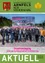 Eine Gruppe von Menschen steht vor einer Baustelle mit einem Werbeschild für das neue Geschäftsgebäude von Elektro Lang. Sie alle lächeln und scheinen für ein Foto zu posieren.