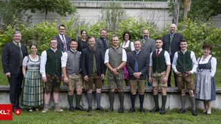 Eine Gruppe von Männern und Frauen in traditioneller bayerischer Kleidung posiert für ein Foto im Garten.
