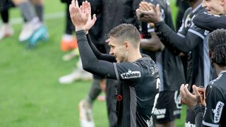 A soccer player celebrates on the field, wearing a black jersey with the number 2, surrounded by teammates clapping.