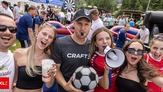 A group of friends, including a man wearing a Craft shirt, are posing with a soccer ball and a cup at an outdoor event.