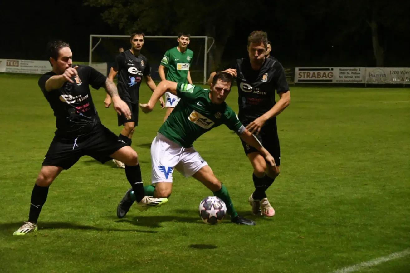 A soccer game at night, players in jerseys with numbers compete on a grass field, one player kicks the ball while others defend.