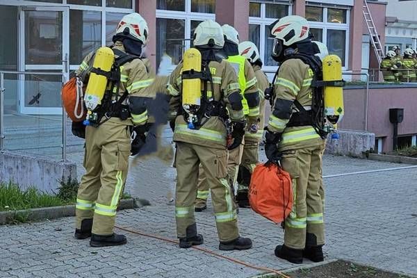 Eine Gruppe von Feuerwehrleuten in voller Ausrüstung steht vor einem Gebäude und bereitet sich auf eine Übung oder einen Notfall vor.