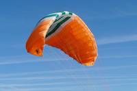 Ein orangefarbener Fallschirm mit grünen und weißen Streifen schwebt in einem blauen Himmel.