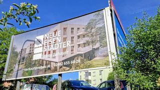 A billboard advertising a new building project called Neue Eisen Stadter, with a contact number 02682 655 60-20, displayed in a scenic setting.