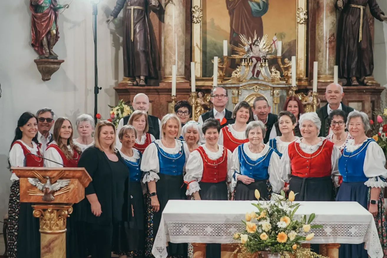 A group of elderly people wearing traditional clothes are posing for a photo in front of an altar in a church.
