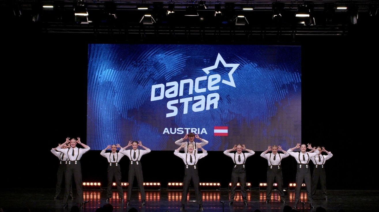 Six dancers perform on stage for Dance Star Austria, with a large screen displaying the show's logo behind them.