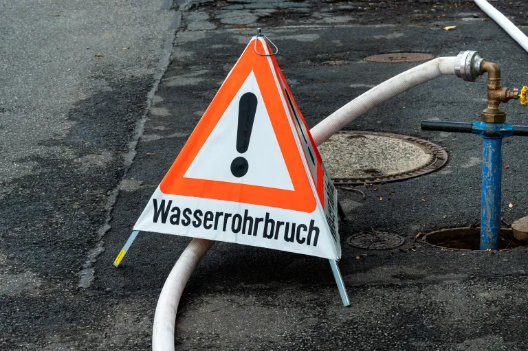 A warning sign for a water pipe break, with a hose lying on the ground.