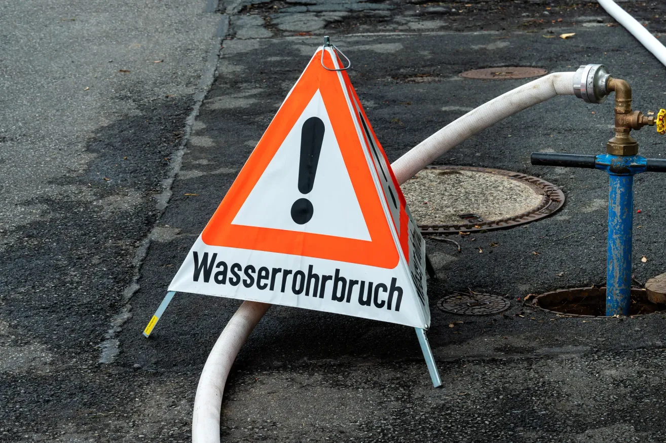 A warning sign for a water pipe break, with a hose lying on the ground.