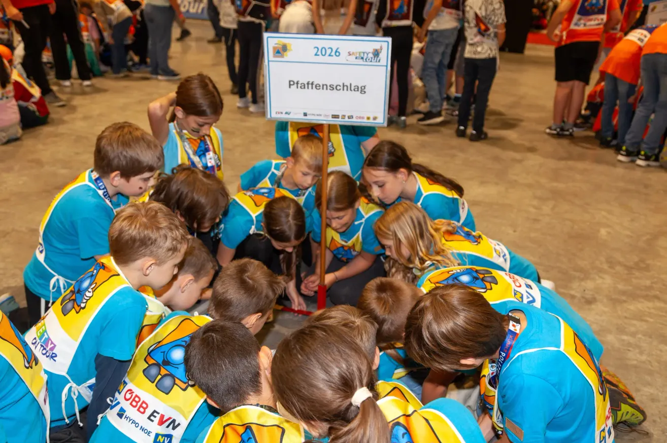 A group of children in matching blue and yellow uniforms are gathered around a whiteboard with the text 2026 Pffaffenschlag. They are likely participating in a team event or competition.