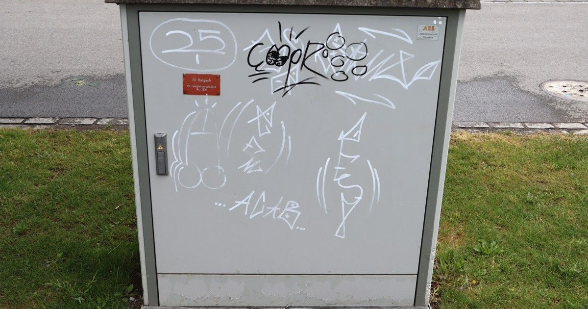 A gray electrical box with graffiti, including '25', 'COPR', and 'ALGB'. It has a red label with 'Ev Baigaah' and 'WK Fernkommunikation'.