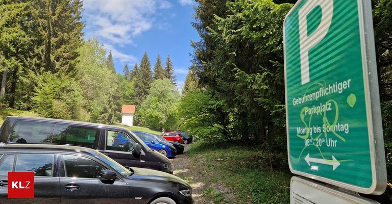 A few cars are parked on the side of a road near a forest with a sign that says 'Parking fee'.