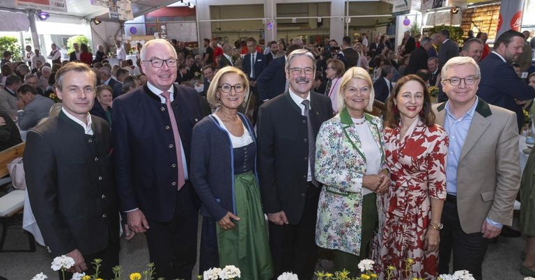 Fünf Personen, drei Männer und zwei Frauen, stehen zusammen in einer formellen Umgebung mit einer Menge im Hintergrund.