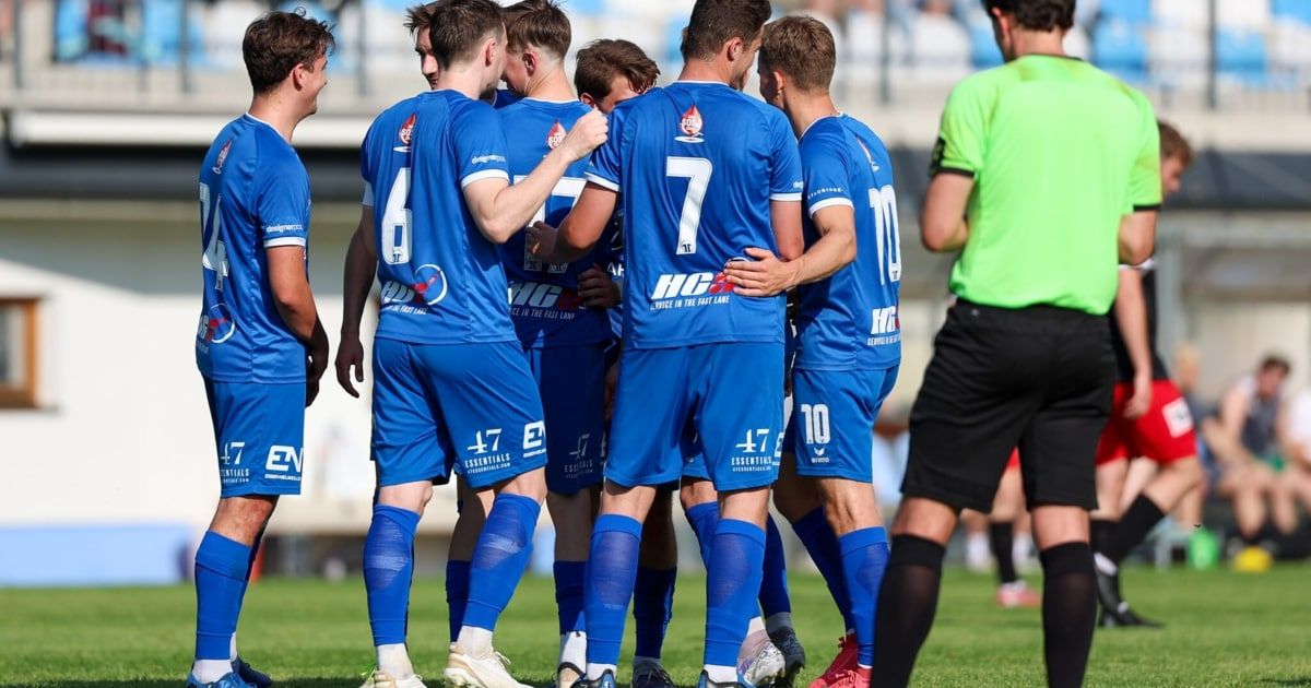 Eine Gruppe junger Fußballer in blauen Trikots steht auf dem Spielfeld versammelt und diskutiert wahrscheinlich ihre Strategie für das Spiel.