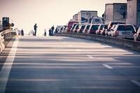 Eine Autobahn mit mehreren geparkten Autos und Lastwagen am Straßenrand, eine Person steht in der Nähe einer Brücke und andere versammeln sich in der Ferne.