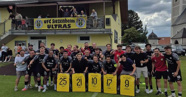 A soccer team poses for a photo in front of a building with a banner reading UFC Siezenheim ULTRAS. They hold yellow signs with numbers 25, 21, 10, 17, and 9.
