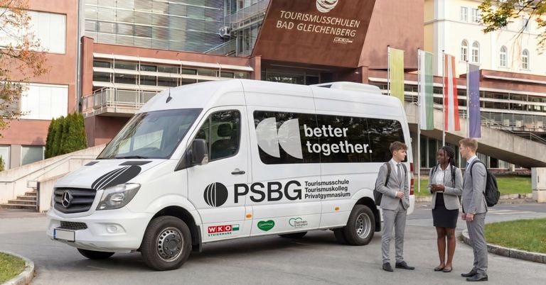 A white van with black accents and the slogan 'better together' is parked in front of a building with the sign 'Tourismusschulen Bad Gleichenberg'. A man and a woman are standing beside the van.