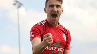 Ein Fußballspieler feiert ein Tor. Er trägt ein rotes Trikot mit weißen Streifen und dem Logo von Holz auf der Brust.